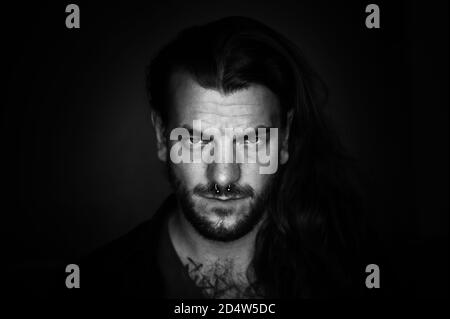 Man with long hair looks seriously and determined at the camera on an black and white image Stock Photo