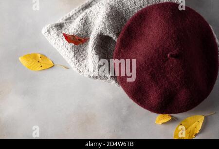 burgundy beret hat and knitted gray scarf on a gray background Stock Photo