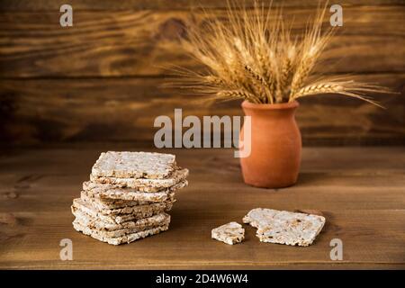 Stack of crusty crispbread on a brown wooden background in close up. Delicious substitute for bread. Healthy dietary product. Ears of wheat in a vase Stock Photo