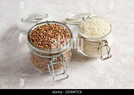 Two glass jars with uncooked rice and buckwheat grains on a light background. Methods of preservation of groats. Healthy food. Storage organic product Stock Photo