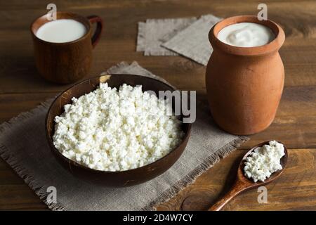 In wooden and clay dishes dairy products cottage cheese, milk, sour cream close up. The bowl stands on a canvas napkin against a dark wooden backgroun Stock Photo