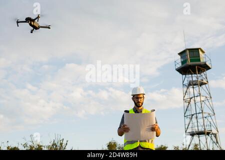 Worker Standing And Checking His Plans next to a flying drone Stock Photo