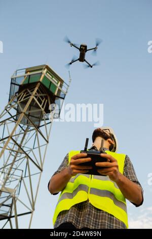 Drone operator man piloting a drone next to a tower Stock Photo