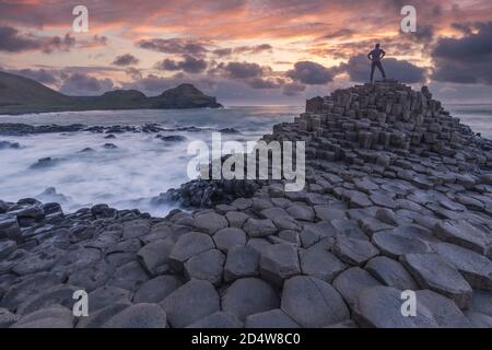 Silhouette of one person standing at Giant Causeway rocks at sunset in Northern Ireland  Stock Photo