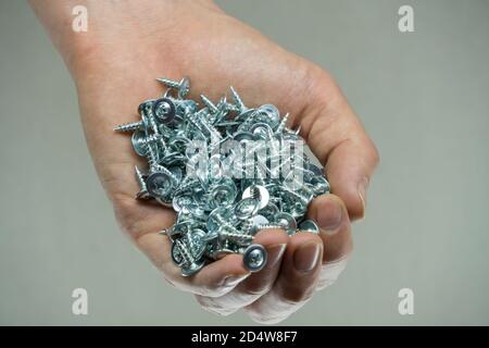 Hold a set of cogs in your hand. Bolts in a man's hand. Screws and cogs. Tools for fixing and repairing. Stainless steel bolts. Galvanized metal faste Stock Photo