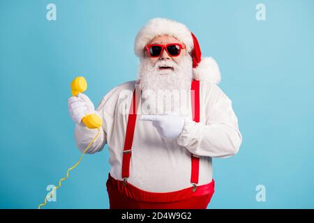 Portrait of his he nice attractive cheerful funky white-haired Santa holding in hand demonstrating yellow retro telephone isolated over bright vivid Stock Photo
