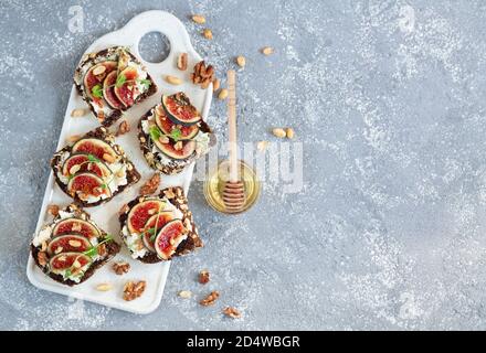 Fig bruschettas with ricotta, nuts and honey on stone table. Flat lay, copy space Stock Photo