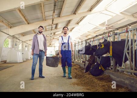 Smiling dairy farm workers standing and looking at camera after feeding cows on typical working day Stock Photo
