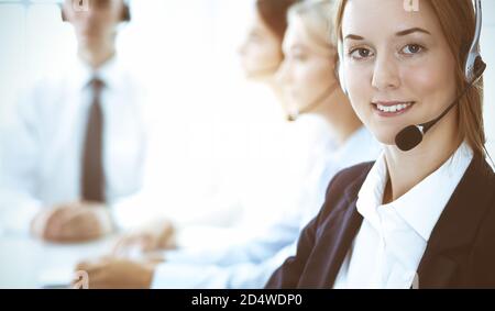 Call center and business people concept. Beautiful business woman with headphones consulting clients. Group of diverse phone operators at work in Stock Photo