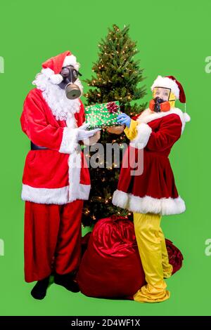 Santa Claus and the Mrs. dressed in ppe, or personal protective gear, including gloves, masks and suits exchanging gifts under Christmas tree with rem Stock Photo