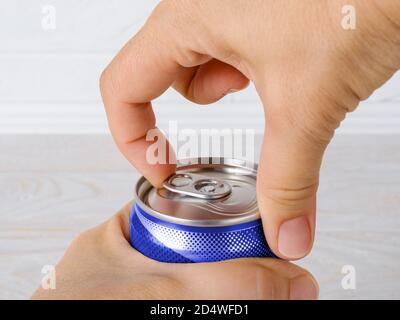Pair of woman hands opening a can of soda or beer close-up. Drinking on the go beverages in aluminum cans with pull tabs. Front view. Stock Photo