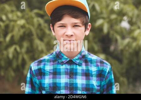 Stylish blond teen boy 14-16 year old over green nature background closeup. Looking at camera. Teenagerhood. Stock Photo