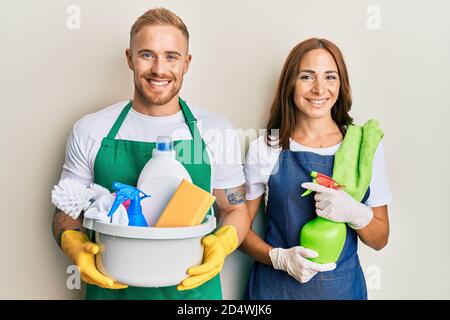Young couple of girlfriend and boyfriend wearing apron holding products and cleaning spray smiling with a happy and cool smile on face. showing teeth. Stock Photo