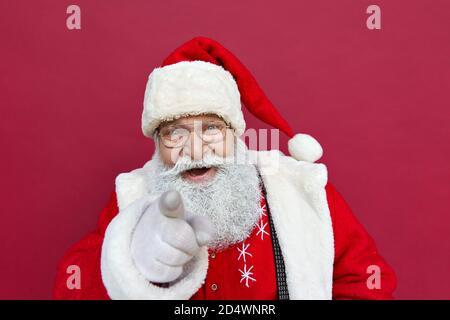 Happy Santa Claus looking at camera pointing finger at you on red background. Stock Photo