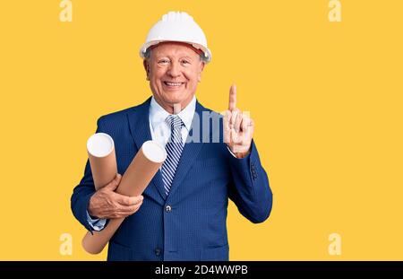 Senior handsome grey-haired man wearing architect hardhat holding blueprints surprised with an idea or question pointing finger with happy face, numbe Stock Photo