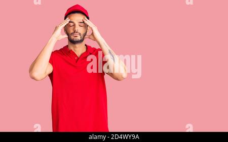 Young handsome hispanic man wearing delivery courier uniform suffering from headache desperate and stressed because pain and migraine. hands on head. Stock Photo