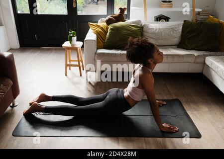Ethnic female teen stretching on yoga mat in modern lounge  Stock Photo