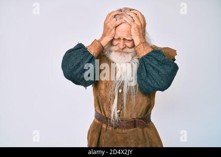 Old senior man with grey hair and long beard wearing viking traditional costume suffering from headache desperate and stressed because pain and migrai Stock Photo