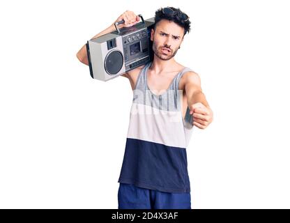 Young hispanic man holding boombox, listening to music annoyed and frustrated shouting with anger, yelling crazy with anger and hand raised Stock Photo
