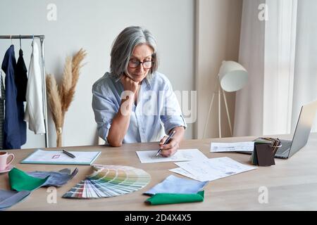 Senior elegant female fashion designer drawing sketches in studio office. Stock Photo