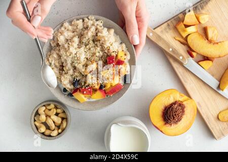 Oatmeal bowl with peach and hemp seeds in female hands. Clean eating, dieting, vegan food concept Stock Photo