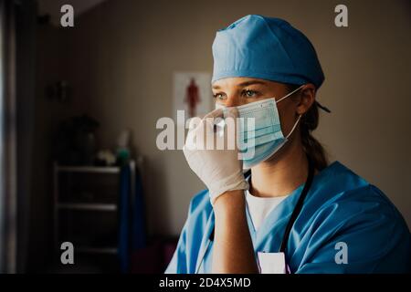 female nurse dressing up in surgical gloves and scrubs preparing to see sick patient in clinic  Stock Photo