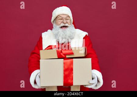 Happy Santa Claus holding presents, laughing, standing on red background. Stock Photo