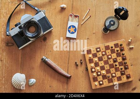 Topview of retro travel equipment on a wooden table. Vintage camera, matches, knife, mussel, chess board and compass on a wooden table. Stock Photo