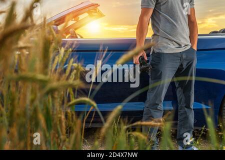Caucasian Tourist in His 40s with Modern Pro Digital Camera in His Hand and Convertible Vehicle Next to Him. Travel Photography Theme. Stock Photo