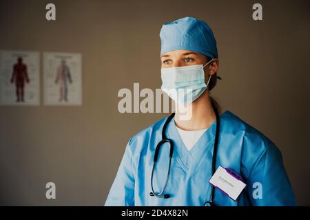 Caucasian female nurse wearing scrubs prepared to see symptomatic patient in doctors clinic