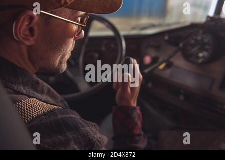Two Way CB Radio Convoy Communication. Caucasian Trucker in His 40s Making Conversation Using Built In Truck Cabin Radio. Transportation and Communica Stock Photo