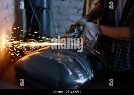 Repairman wearing checked shirt grinding motorbike fuel tank part Stock Photo