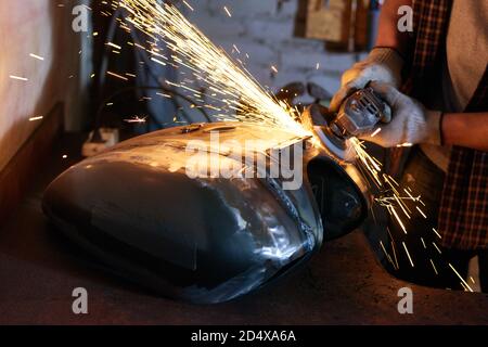 Man wearing checked shirt and protective gloves grinding motorbike fuel tank Stock Photo
