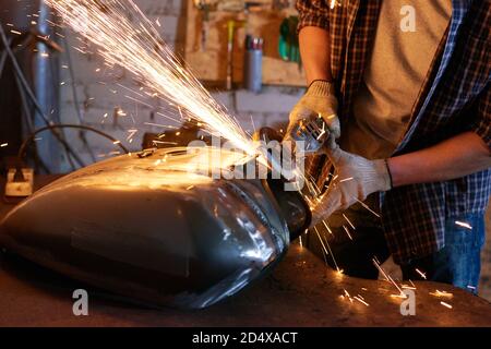 Unrecognizable man using grinder repairing motorcycle fuel tank Stock Photo