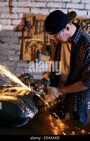 Repairman grinding motorbike fuel tank in his workshop medium Stock Photo