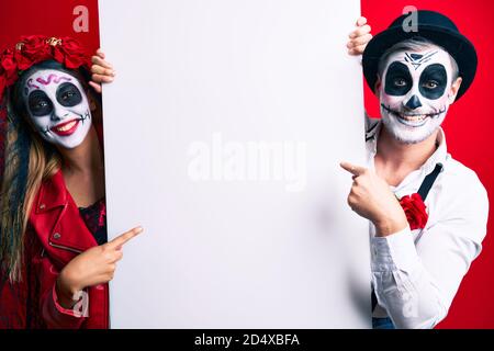Couple wearing day of the dead costume holding blank empty banner smiling happy pointing with hand and finger Stock Photo