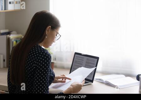 Focused young woman in eyeglasses reading paper document. Stock Photo