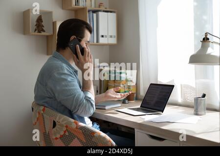Young man working on computer with documents, talking on phone. Stock Photo
