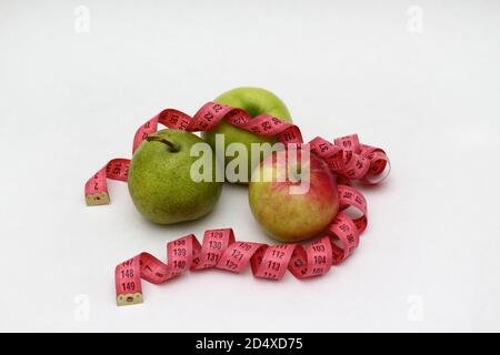 Two fresh green and red apples and green pearlie with pink measuring ribbon on white background Stock Photo