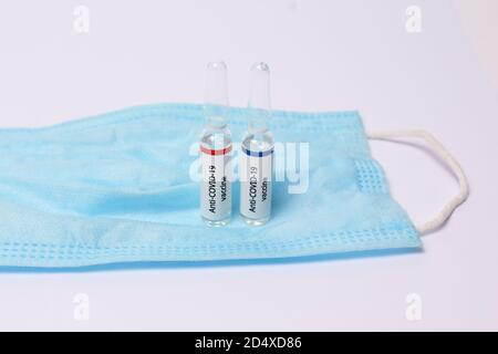 Two medicine ampule with anti covid-19 vaccine on protection mask on white background Stock Photo