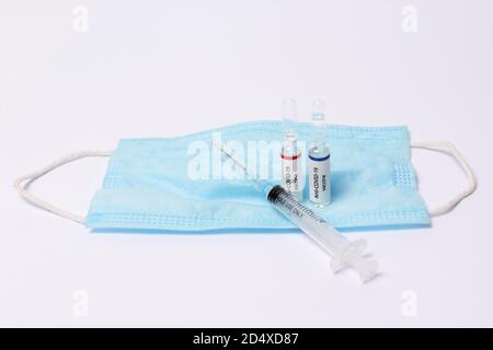 Two medicine ampule with anti covid-19 vaccine and syringe on protection mask on white background Stock Photo