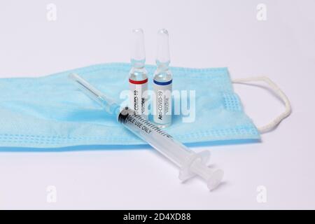 Two medicine ampule with anti covid-19 vaccine and syringe on protection mask on white background Stock Photo