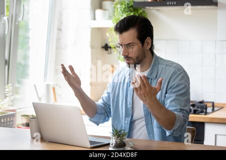 Frustrated angry young man in eyeglasses looking at laptop screen. Stock Photo
