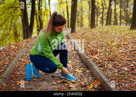 Runner tying shoe laces in autumn park. Woman training with water bottle. Active healthy sportive lifestyle Stock Photo