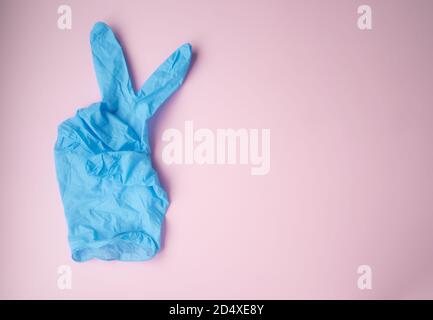 The V mark is shown with a blue medical glove on a pink background. Victory symbol. Defeating the virus. Stock Photo