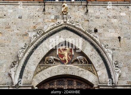 Arched portal of Palazzo Pubblico in Piazza del Campo with the Sienese and the Capitoline Wolf on the sides of the coat of arms, Siena, Tuscany, Italy Stock Photo
