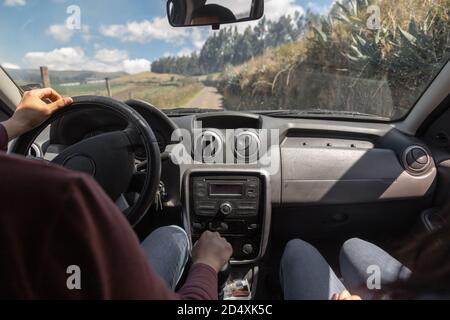 interior of a car, showing the dashboard, steering wheel, windshield and person driving with a passenger, in the background is a countryside landscape Stock Photo