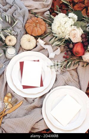 Autumn table setting with golden cutlery, olive branches and porcelain plates. Pumpkins and pomegranate fruit. Blank cards mockups. Fall, Thanksgiving Stock Photo