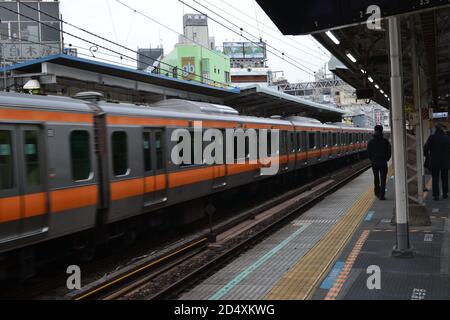 Tokyo, Japan-02/23/16: People walking along the train platform as the local train travels down the rail line at a great speed. Stock Photo