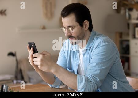 Pleased young handsome man using mobile application at home. Stock Photo